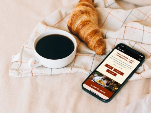 Bild på en kopp kaffe, en croissant och en mobiltelefon som besöker webbplatsen för Frimans i Jönköping. Balowie har varit med och utvecklat hemsidan i CMS:et Kirby