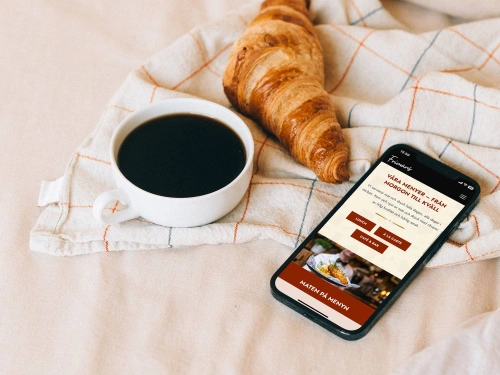 Bild på en kopp kaffe, en croissant och en mobiltelefon som besöker webbplatsen för Frimans i Jönköping. Balowie har varit med och utvecklat hemsidan i CMS:et Kirby